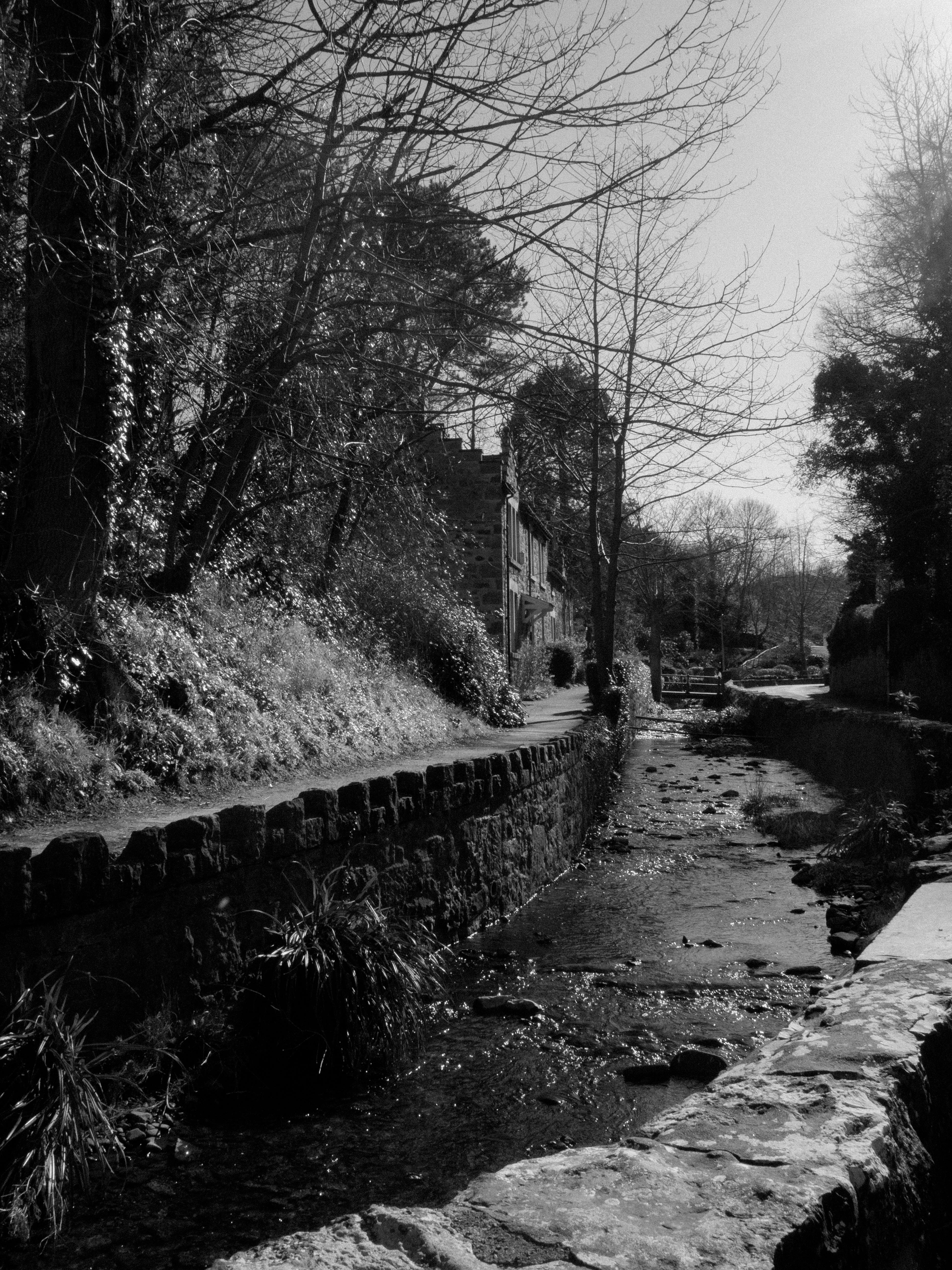 A tranquil countryside stream flows past rustic stone walls in this black and white photo.