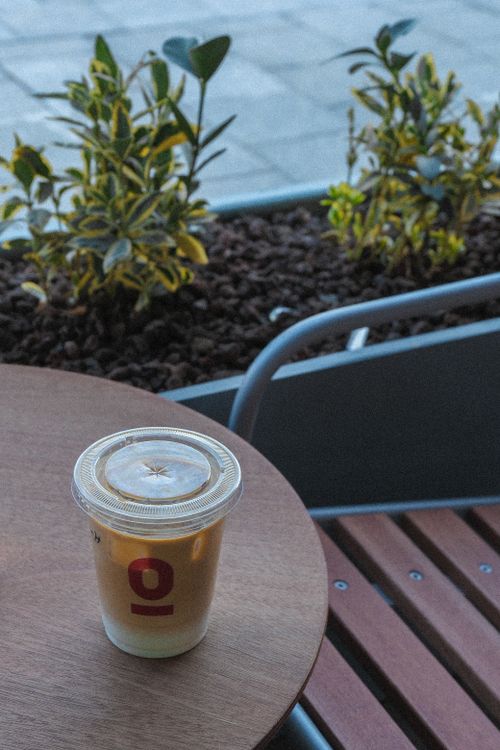 Free A chilled coffee in a plastic cup resting on a wooden table outside a café with plants. Stock Photo
