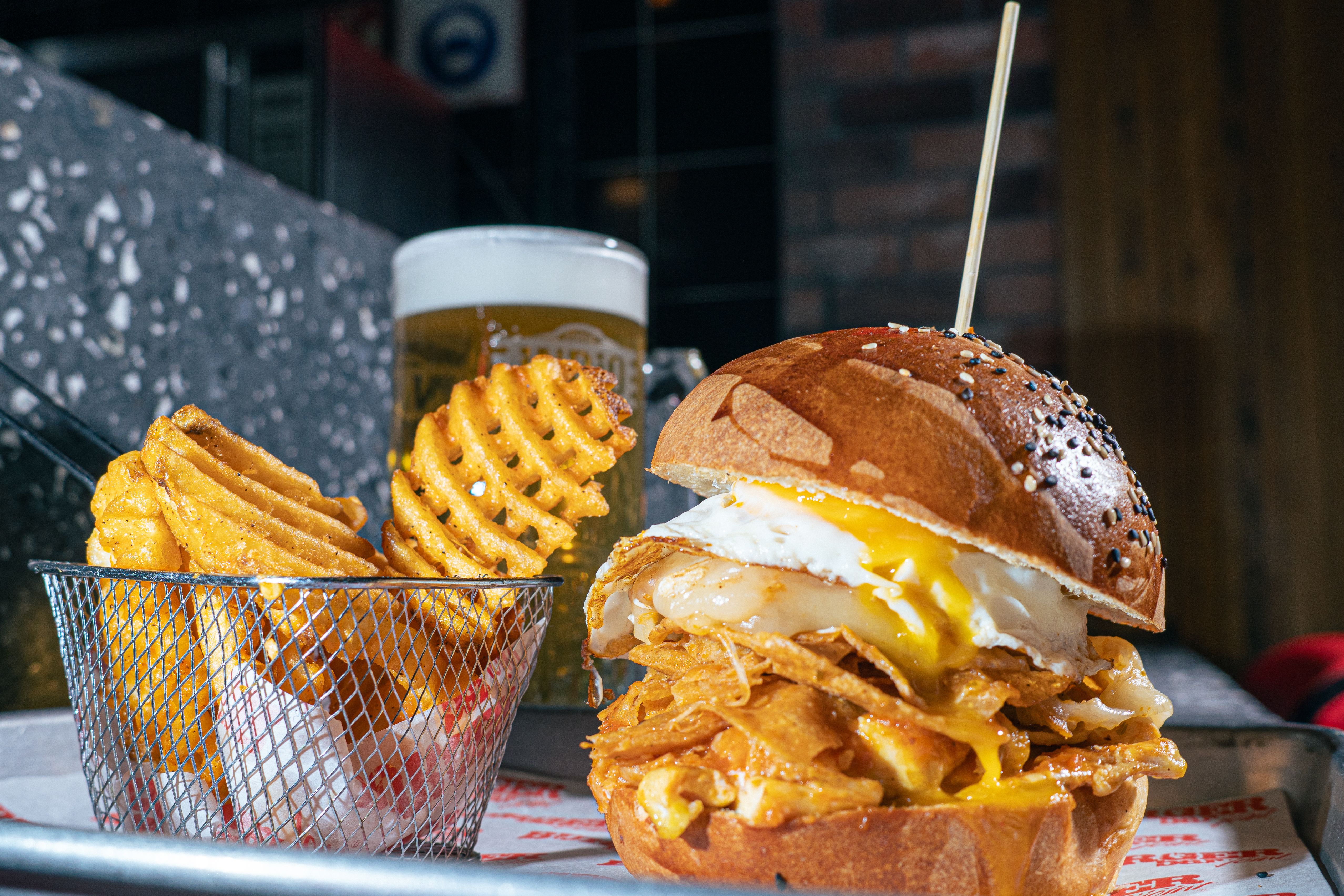 Delicious gourmet burger with waffle fries and a draft beer on a restaurant table.