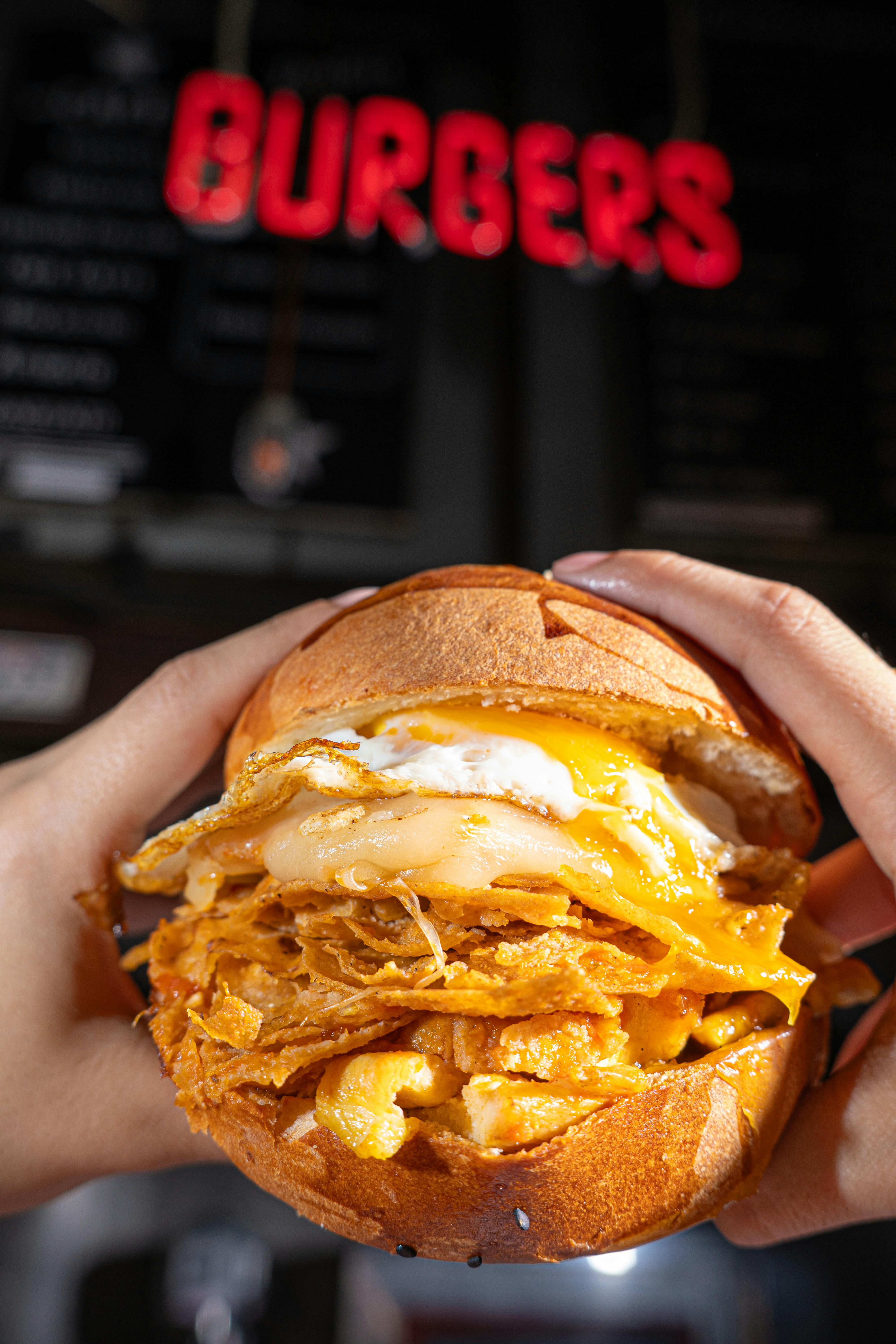 Delicious cheesy fried chicken burger topped with a fried egg, held in hands.