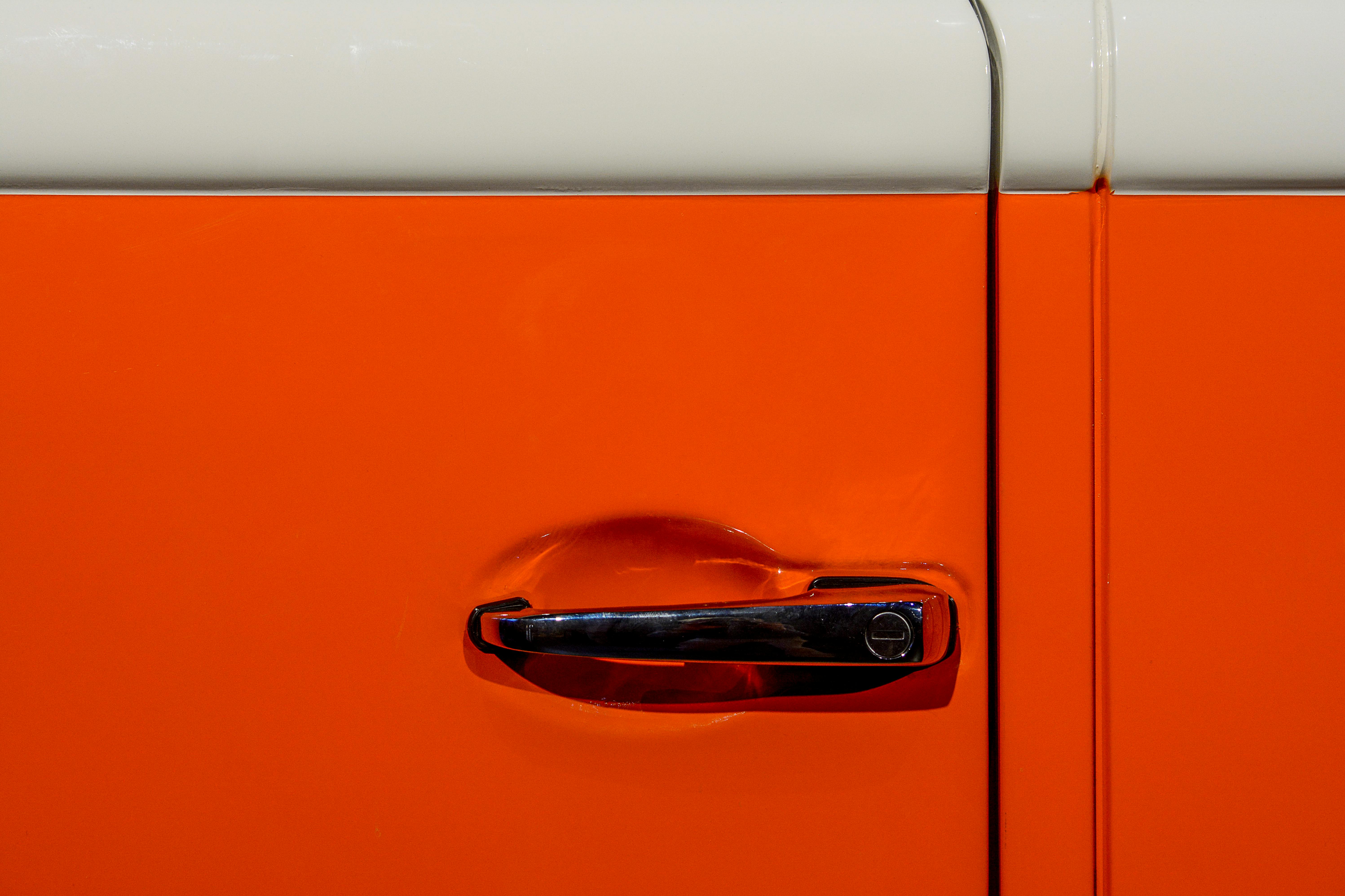 Close-up view of a vintage orange car door handle with shiny chrome detail.