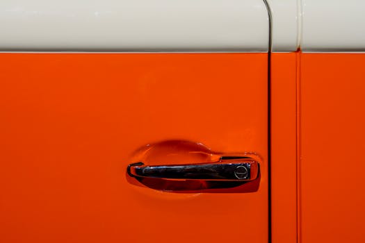 Close-up view of a vintage orange car door handle with shiny chrome detail.