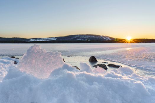 Beautiful winter sunrise over a snowy landscape with ice and distant hills.