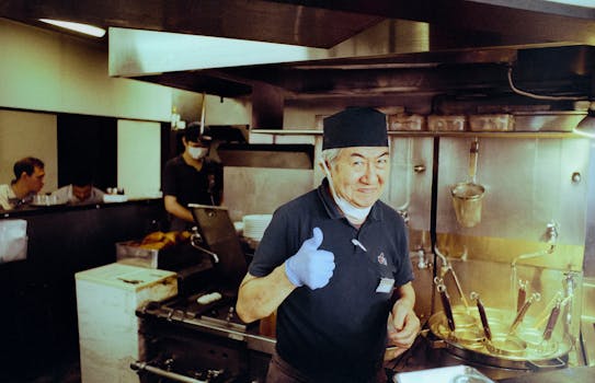 Cheerful chef giving thumbs up in a traditional Japanese ramen restaurant kitchen.