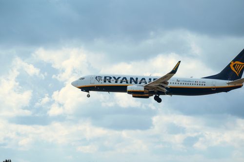 Free Ryanair airplane in mid-air cruising against a vibrant cloudy sky. Stock Photo