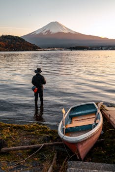 A fisherman stands at Lake Kawaguchi, Yamanashi, with Mount Fuji in the background during sunset.