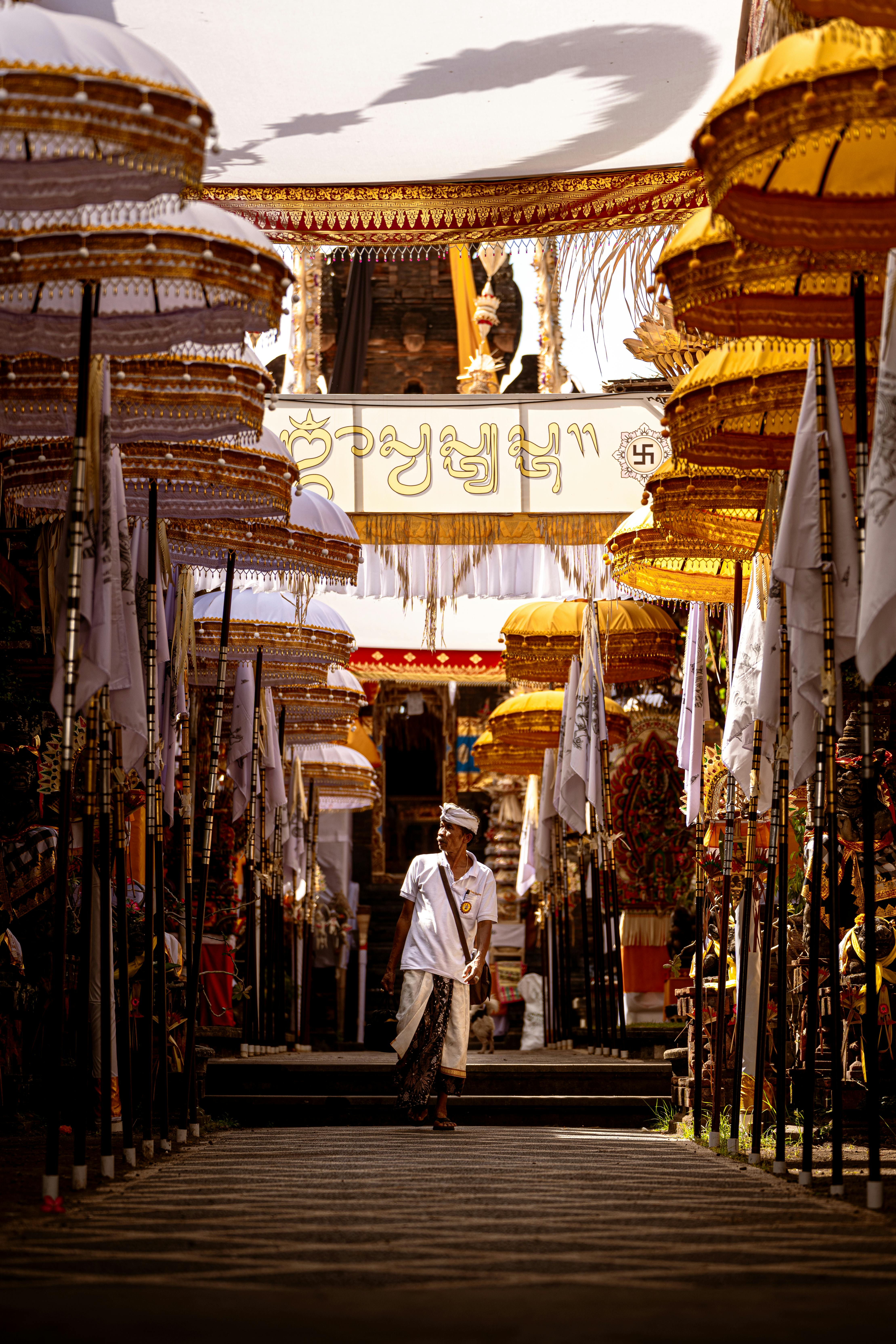 A Balinese priest participates in a vibrant temple ceremony with ceremonial flags and umbrellas.