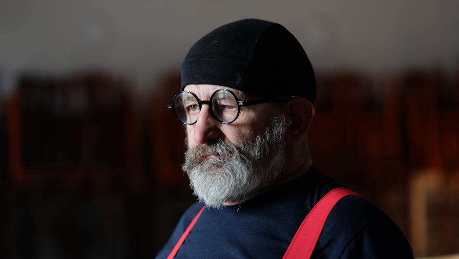 Portrait of a bearded man wearing glasses and a hat, deep in thought.