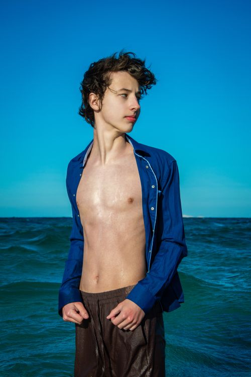 Free Teenage boy standing confidently by the ocean under a clear blue sky. Stock Photo