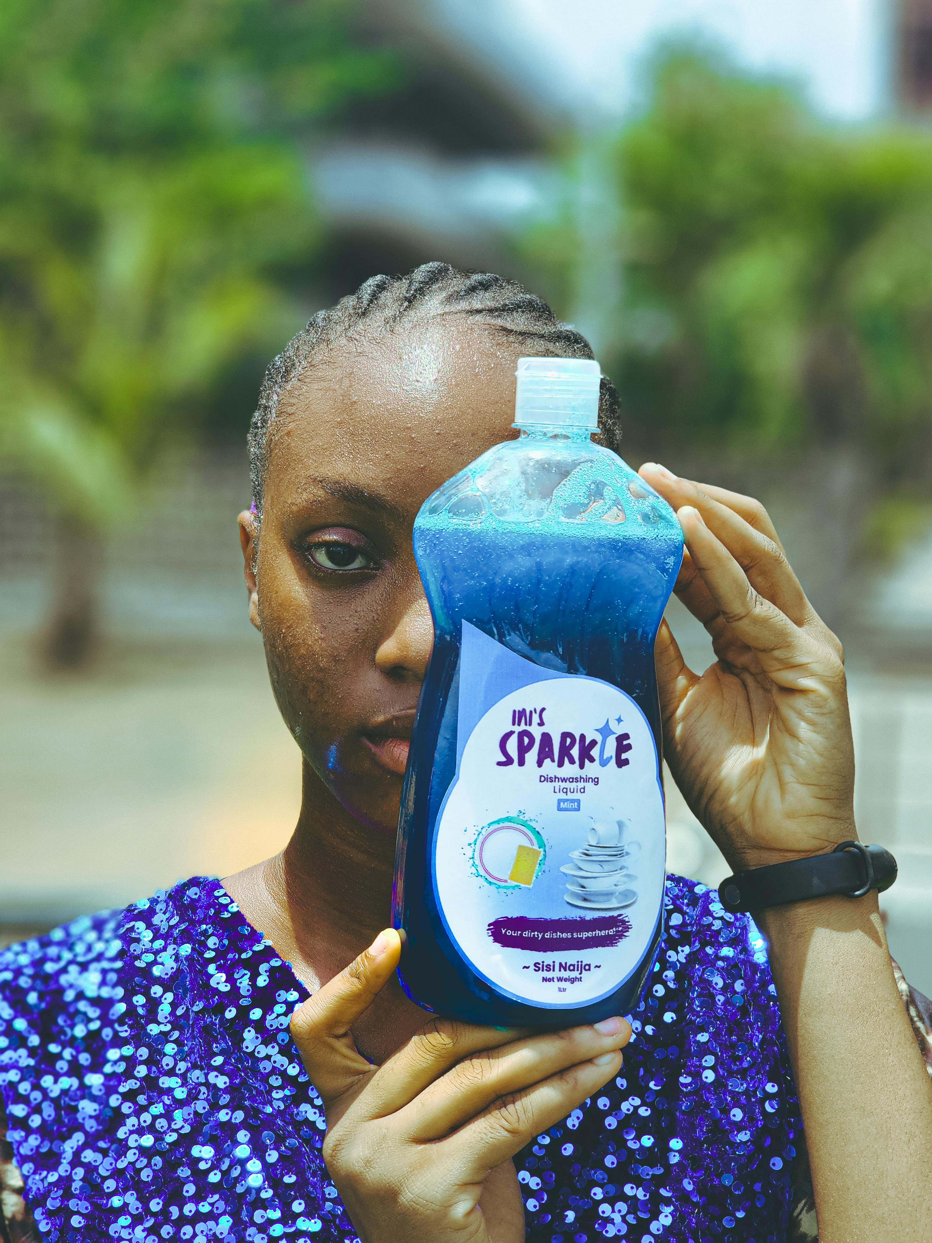 A young woman holding a blue detergent bottle in a tropical setting.
