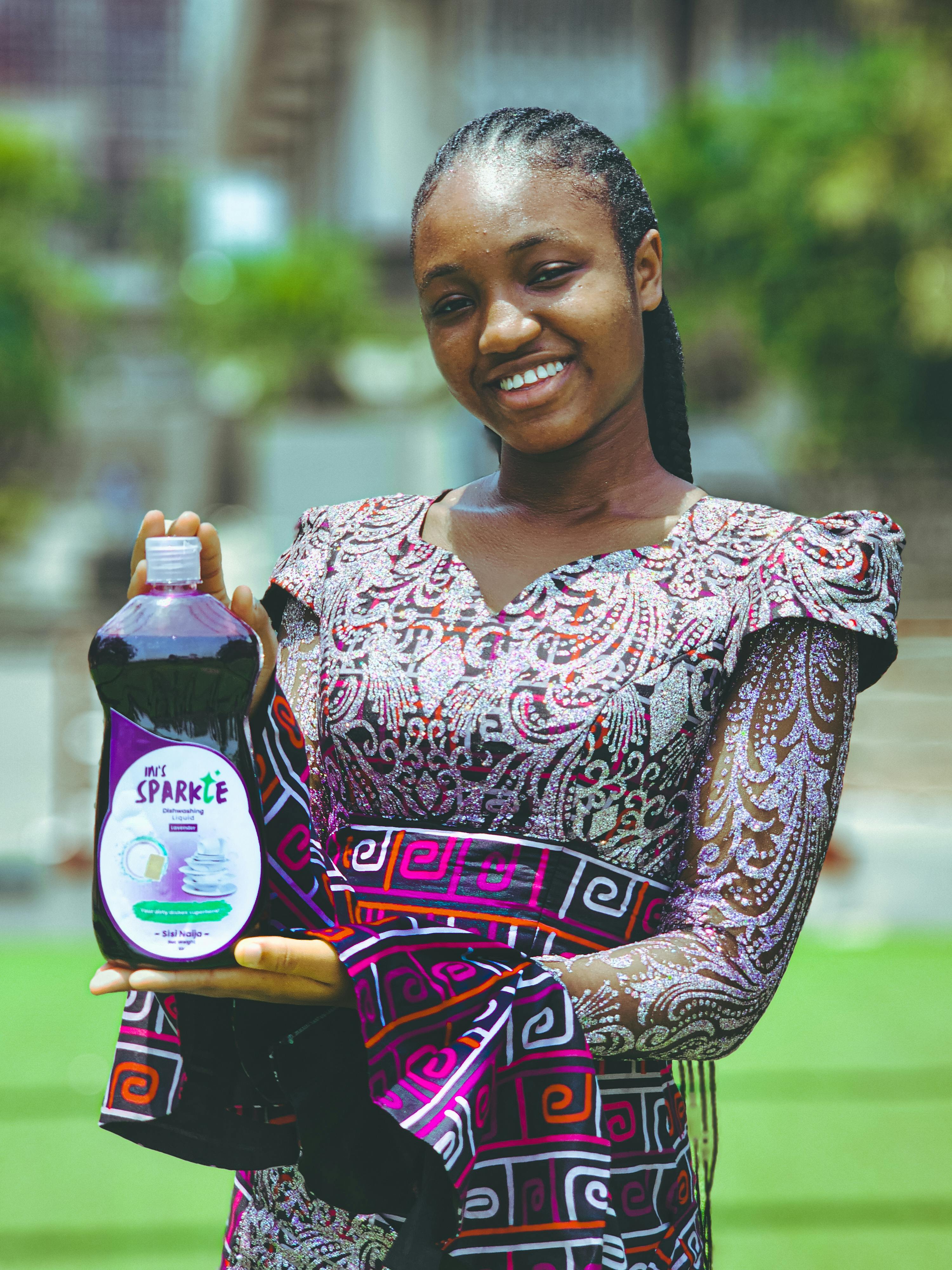 Woman smiling while holding Sparkle cleaning liquid outdoors.