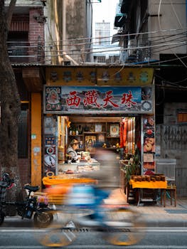 A bustling Asian street scene with a vibrant, colorful market stall and motion blur of a cyclist passing by.
