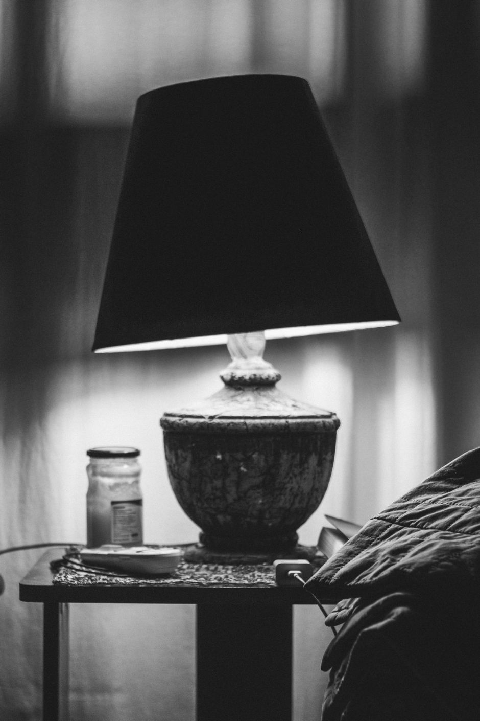 Black and white image of a vintage lamp on a bedside table creating a cozy ambiance.