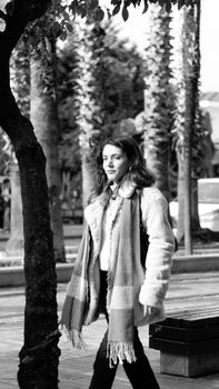 Black and white photo of a woman walking confidently in an urban park.