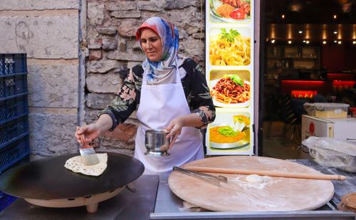 Free Elderly woman making traditional flatbread on griddle at outdoor food stall. Stock Photo