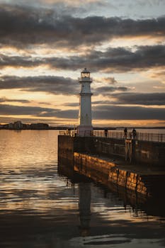 Breathtaking view of a lighthouse at sunset in Edinburgh, Scotland, reflecting on calm waters.