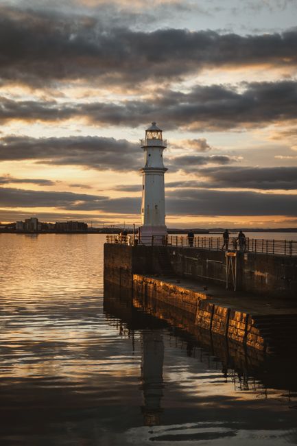 Breathtaking view of a lighthouse at sunset in Edinburgh, Scotland, reflecting on calm waters.