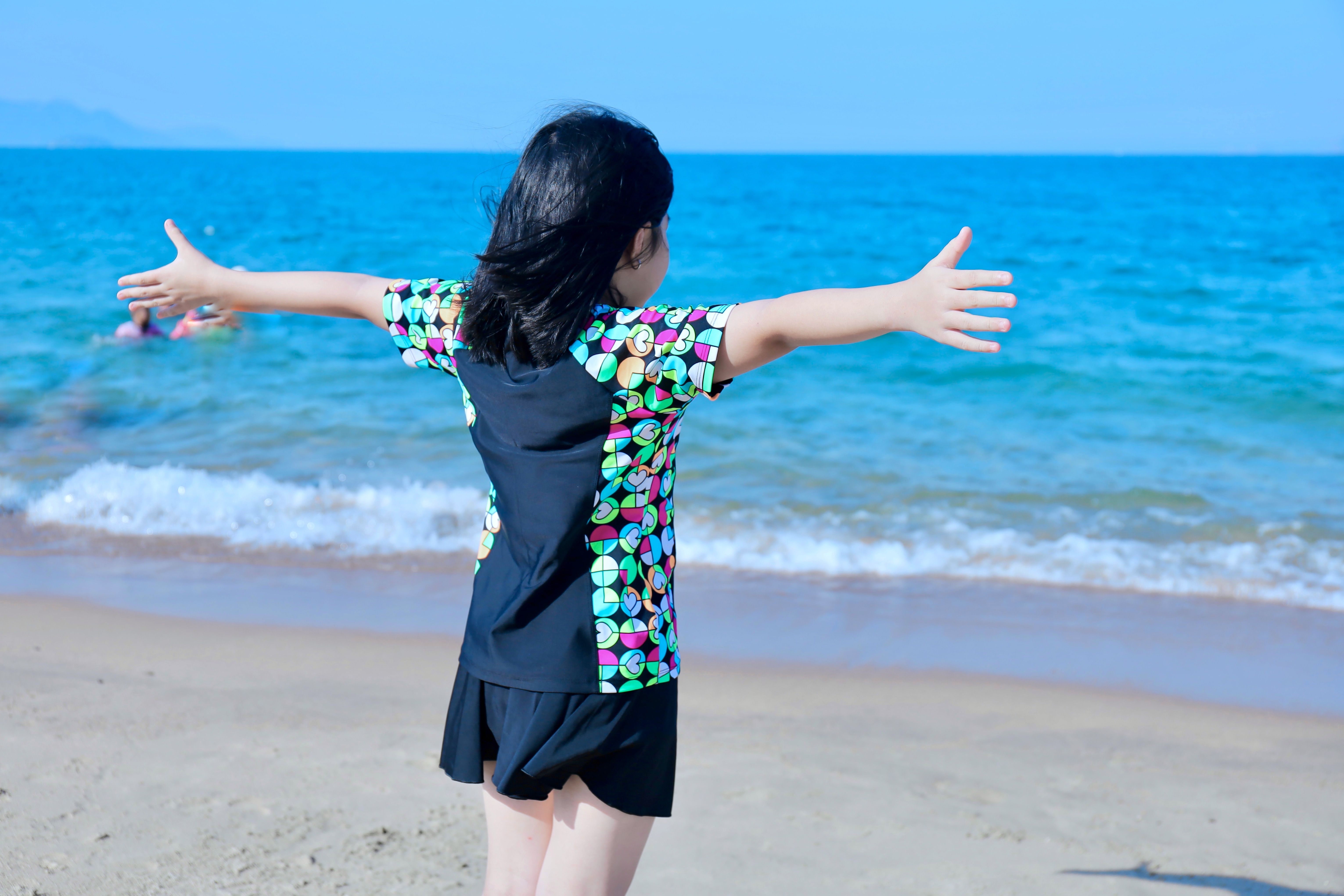 A child with arms outstretched enjoying a sunny day at the beach.