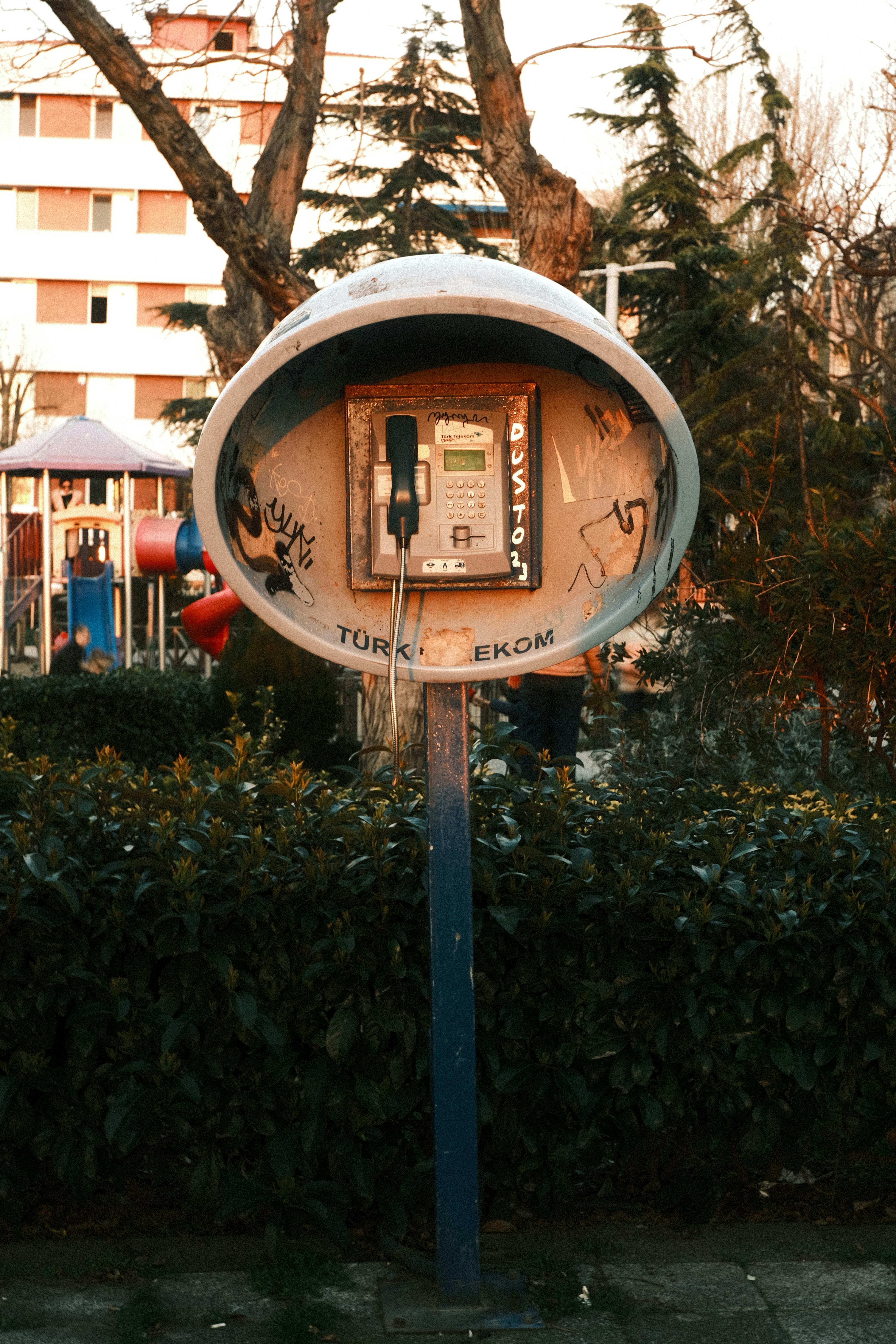 ฟรี โทรศัพท์สาธารณะสไตล์ชนบทตั้งอยู่ท่ามกลางสวนสาธารณะที่เต็มไปด้วยชีวิตชีวาในเมืองอิสตันบูล ประเทศตุรกี ขณะพระอาทิตย์ตกดิน คลังภาพถ่าย