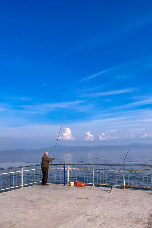 Free A man enjoys peaceful fishing on a pier with a vast ocean view and clear blue skies. Stock Photo