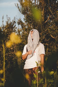 一个人用衬衫遮住脸，站在植物环绕的自然环境中