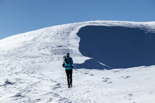 A solo hiker in winter gear trekking a snowy mountain under clear blue skies.