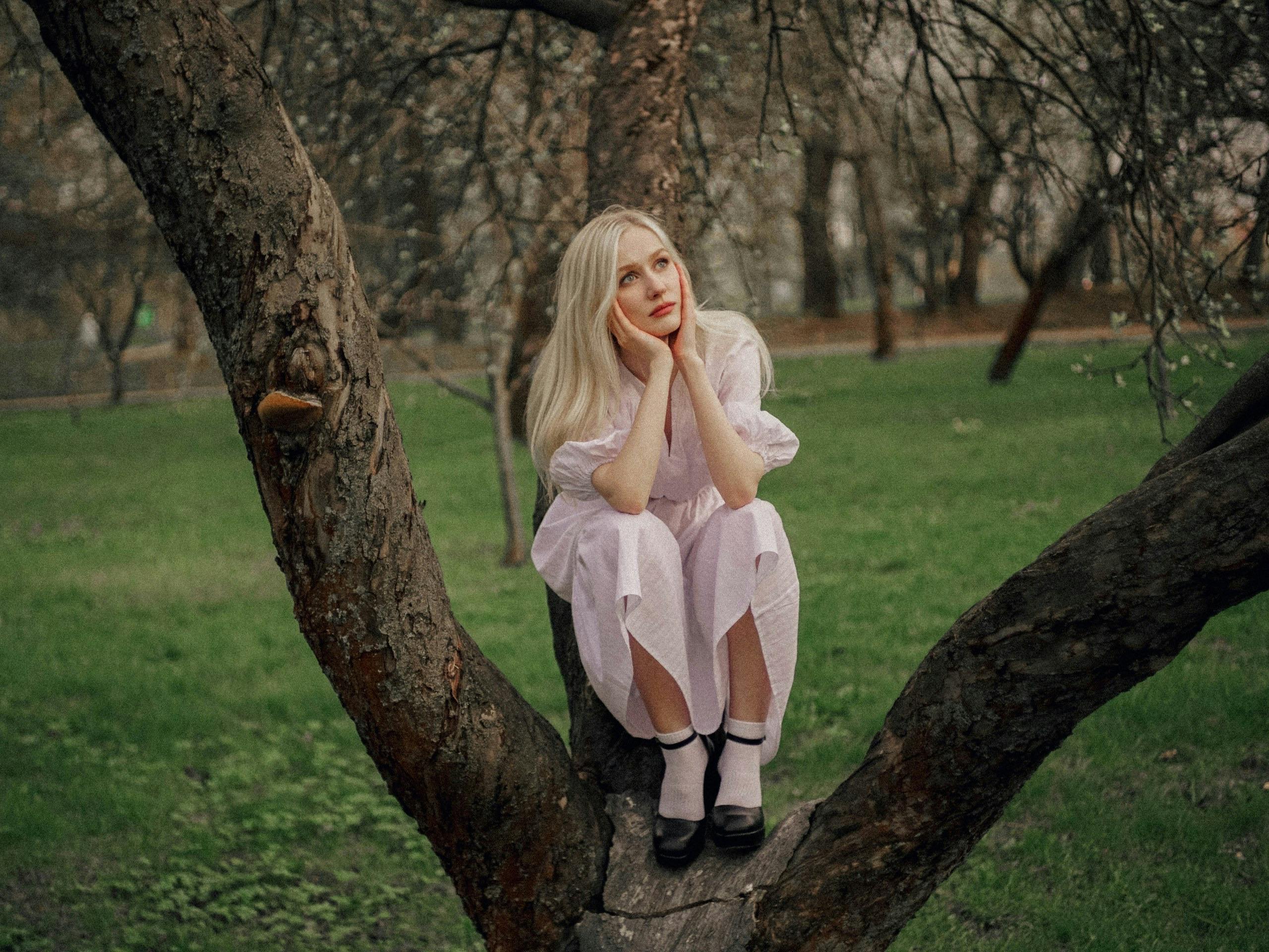 ingyenes Fehér ruhás nő elgondolkodva ül egy fán a buja moszkvai parkban. Stockfotó