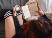 女人坐在沙发上，一边喝着咖啡，一边翻开书读，营造出舒适的室内氛围