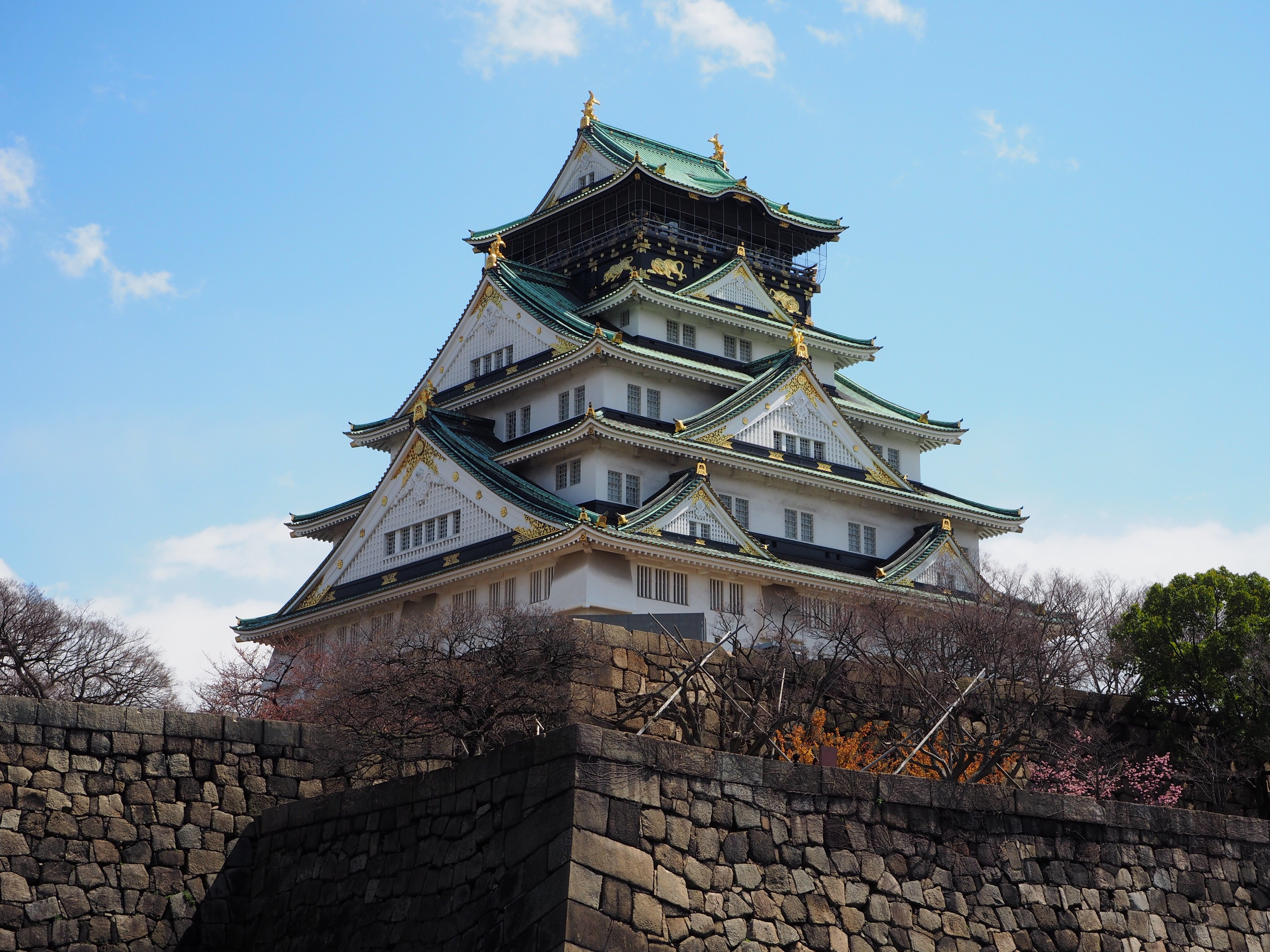 Historic Osaka Castle surrounded by spring foliage under a clear blue sky.