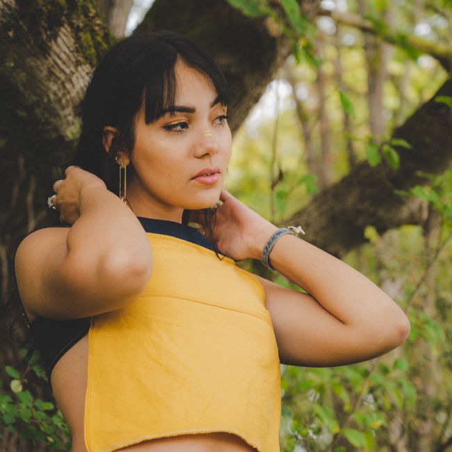 Woman in yellow crop top among trees, embracing summer fashion and nature.