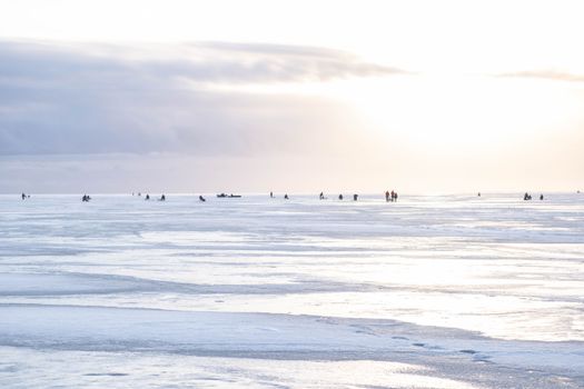 People ice fishing on the frozen sea during a bright winter sunset in Pärnu, Estonia.