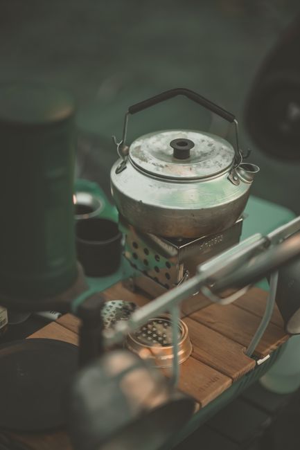Flat lay of camping essentials on a picnic table: stove, headlamp, tent stakes, water bottle, and map