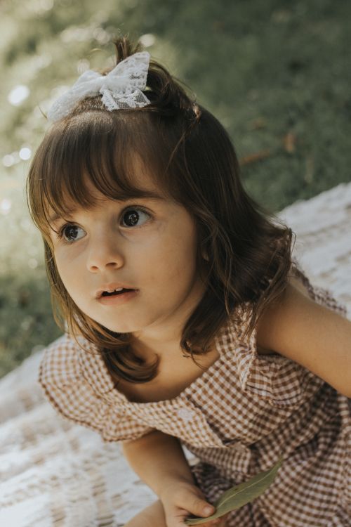 Free Adorable young girl with a bow in hair enjoying a sunny day outdoors. Stock Photo
