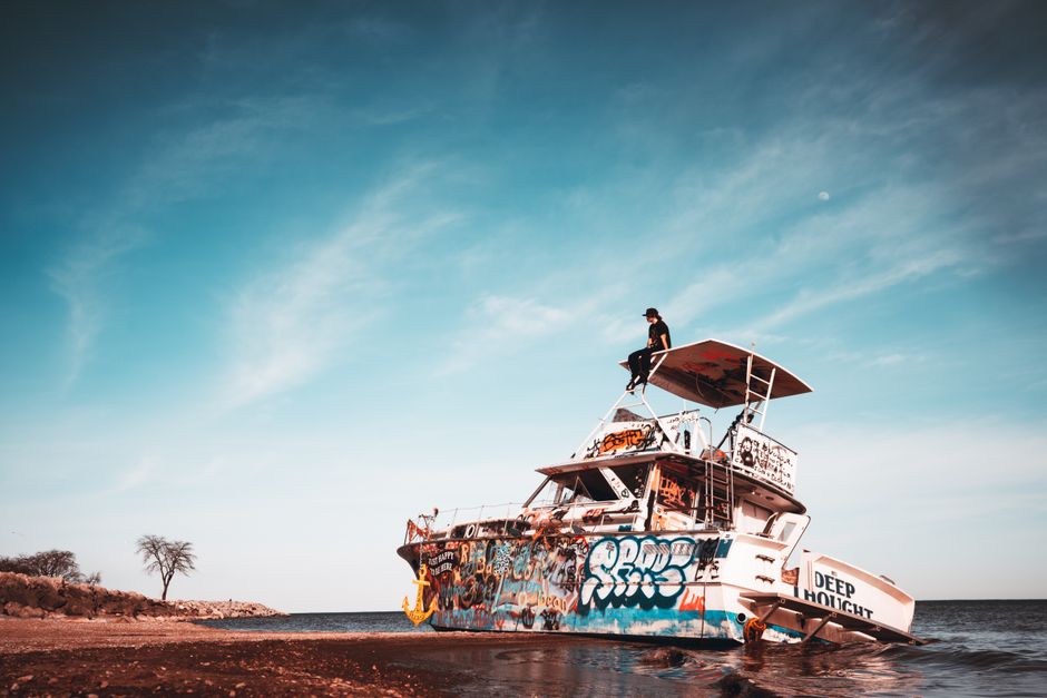 Abandoned shipwreck with graffiti art on Lake Michigan, with person atop during sunrise.