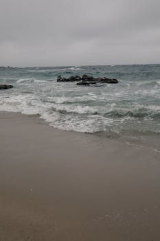Peaceful sandy beach with crashing waves and overcast sky, ideal for serene themes.