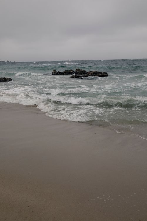 Free Peaceful sandy beach with crashing waves and overcast sky, ideal for serene themes. Stock Photo