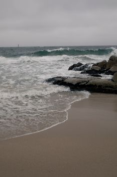 Tranquil ocean waves hitting rocky shore on a cloudy day.