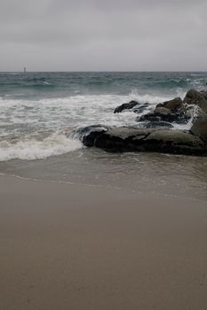 Peaceful seaside scene of waves hitting rocks on a sandy beach.