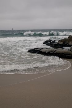 Calm ocean waves gently crash onto a rocky beach under overcast skies, creating a tranquil seascape.
