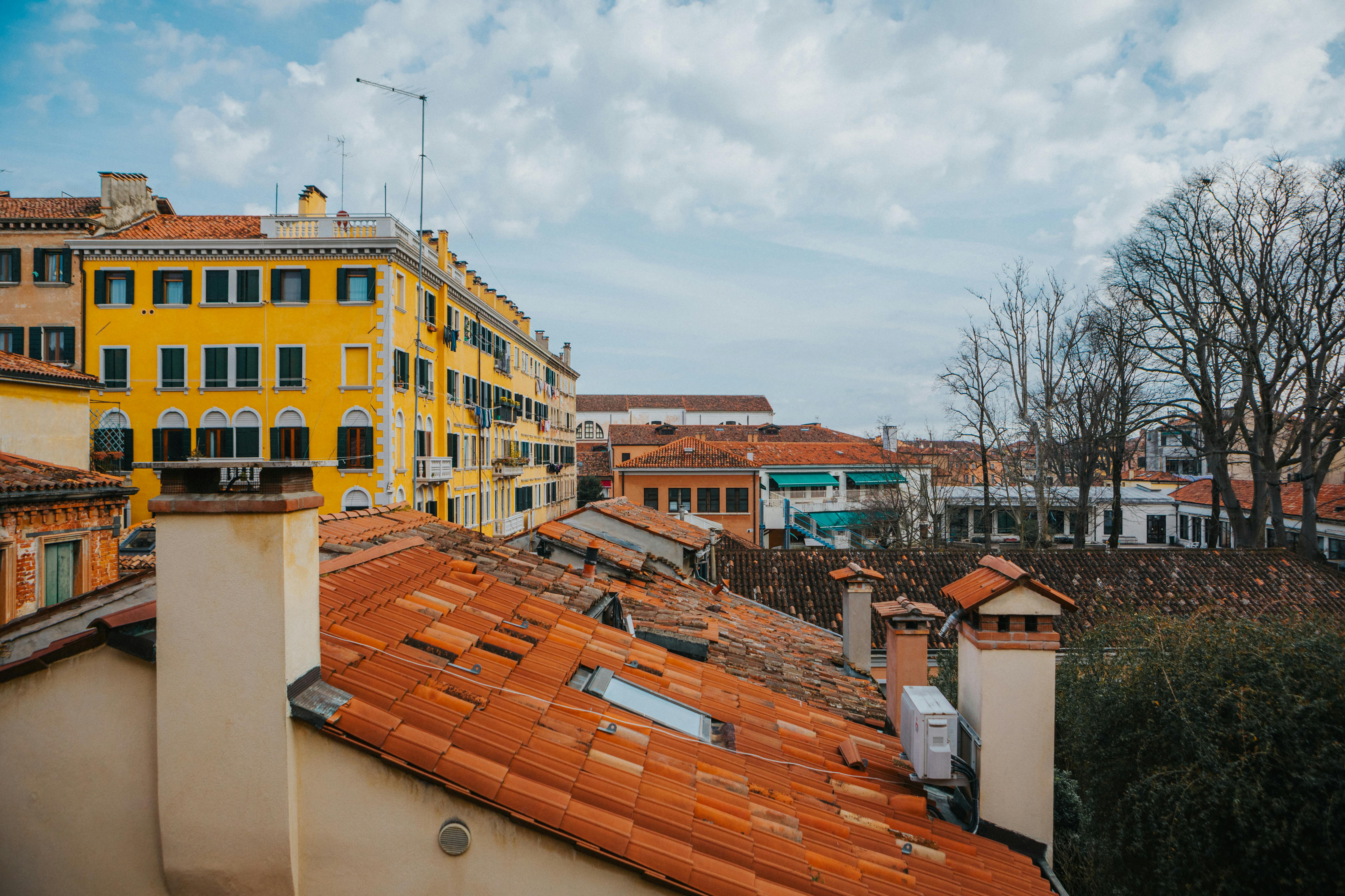 Vue panoramique sur les toits vénitiens avec des bâtiments jaune vif et un ciel nuageux.