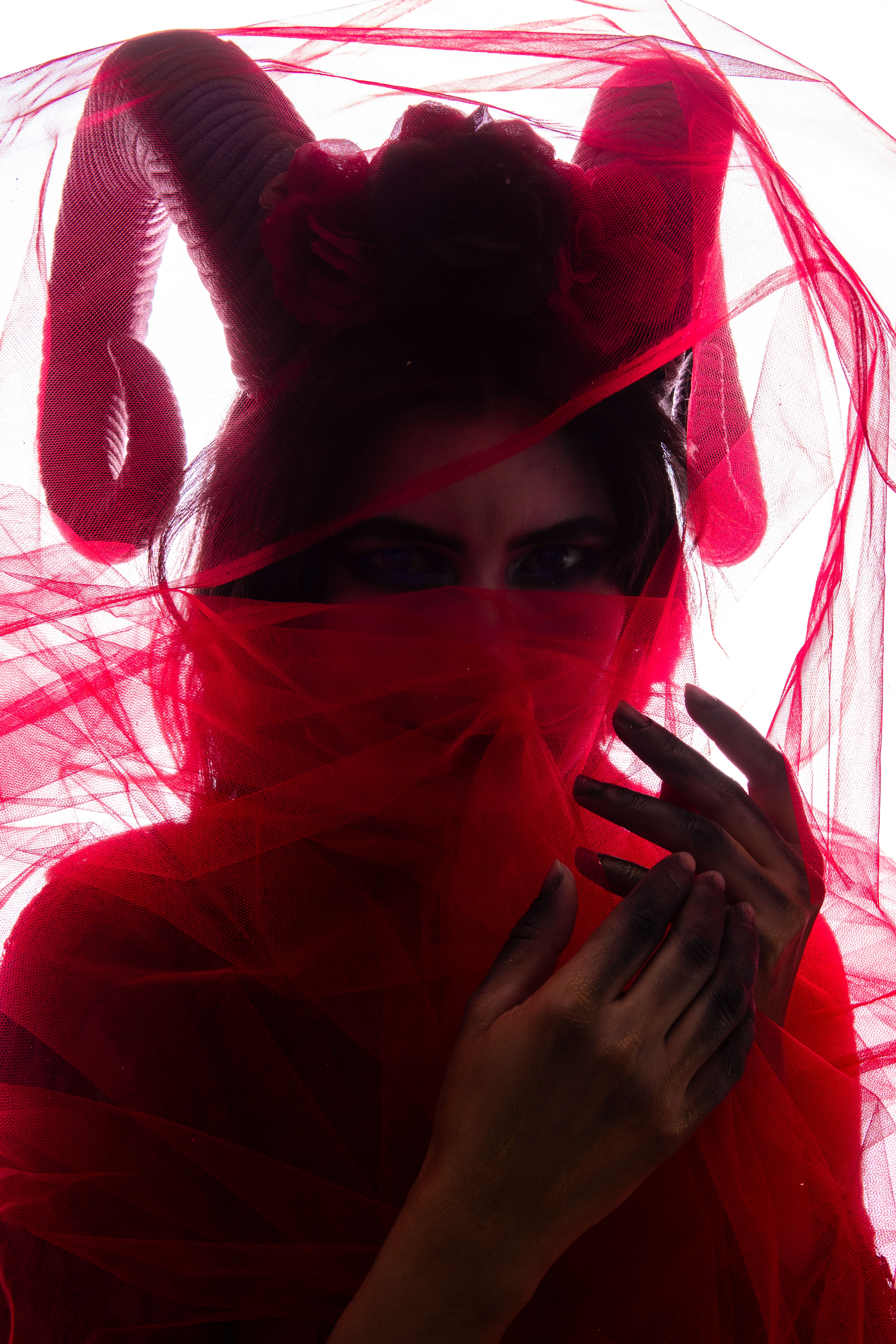 Mysterious fashion portrait of a woman draped in red tulle with a fantasy headpiece.