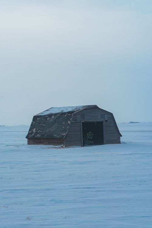 Free A lone barn stands in a vast snowy field under a clear winter sky, exuding solitude and tranquility. Stock Photo