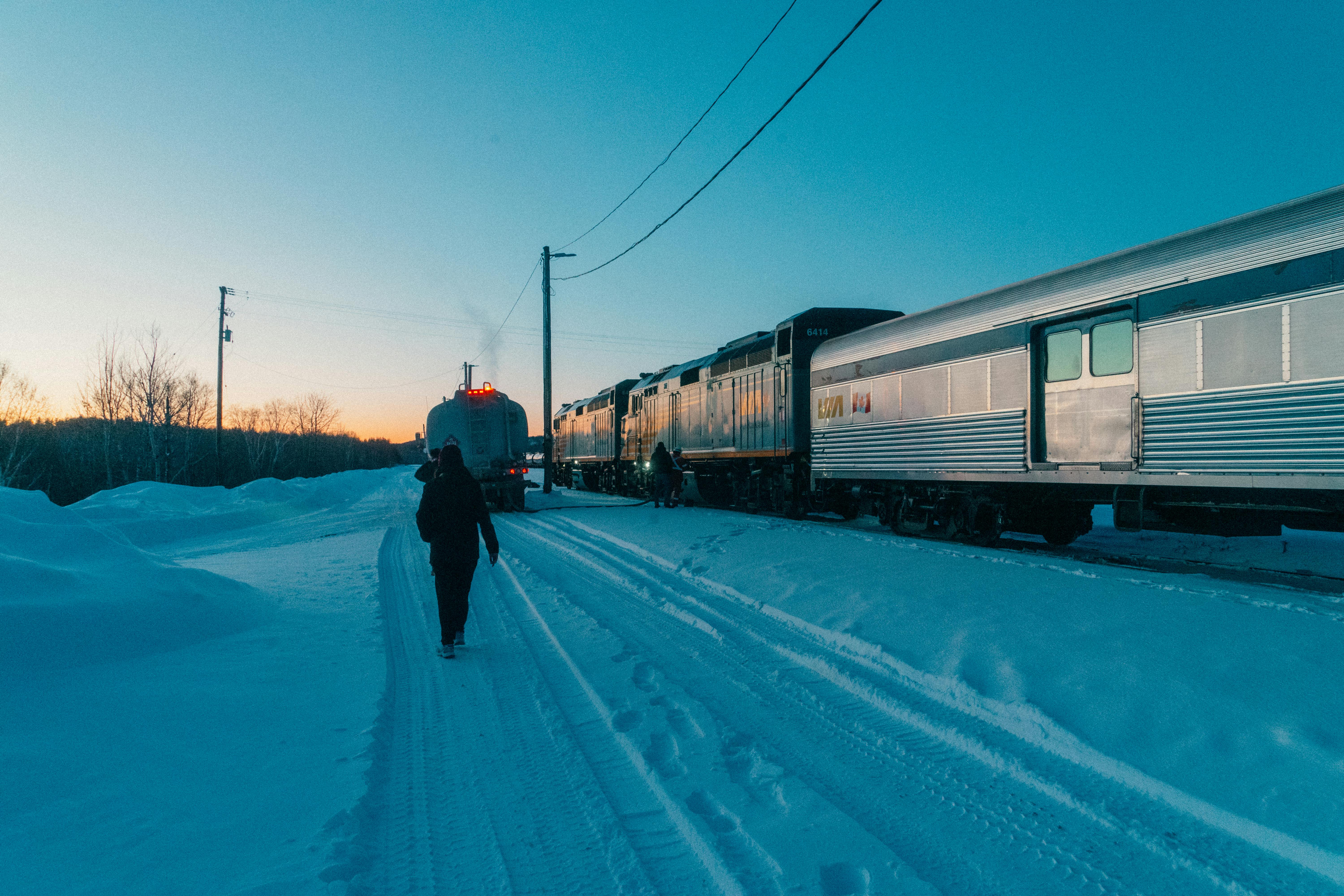 A person walking alongside a snowy train crossing during a picturesque winter sunset in Canada.