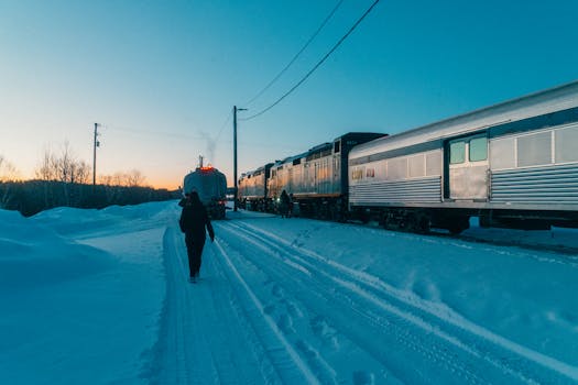 A person walking alongside a snowy train crossing during a picturesque winter sunset in Canada.