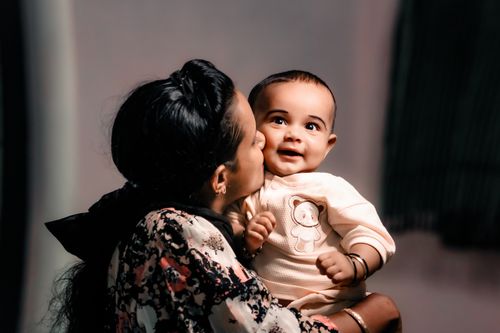 Free A heartwarming image of a mother kissing her smiling baby in a warm embrace. Stock Photo