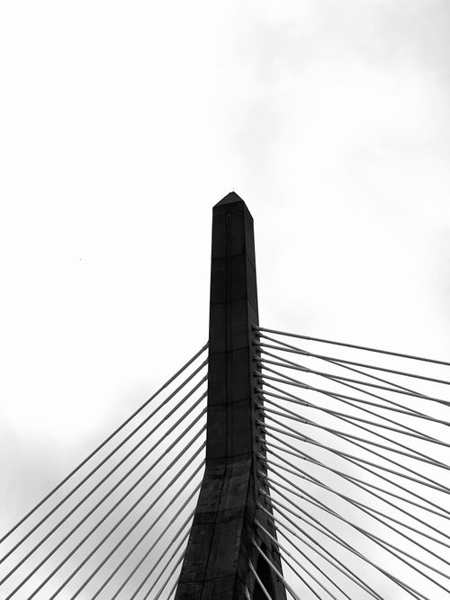 Free A striking black and white image of a modern suspension bridge tower against a cloudy sky. Stock Photo
