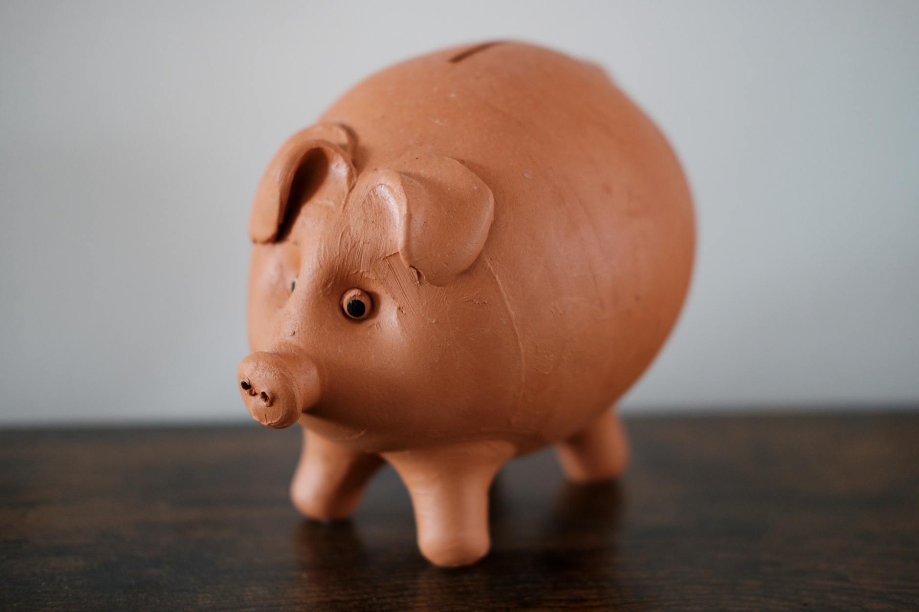 Close-up of a terracotta piggy bank on a wooden table, symbolizing savings.