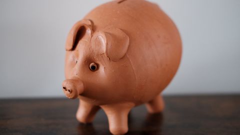 Close-up of a terracotta piggy bank on a wooden table, symbolizing savings.