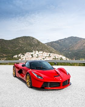 Red sports car parked on a scenic mountainous road with a clear sky backdrop.