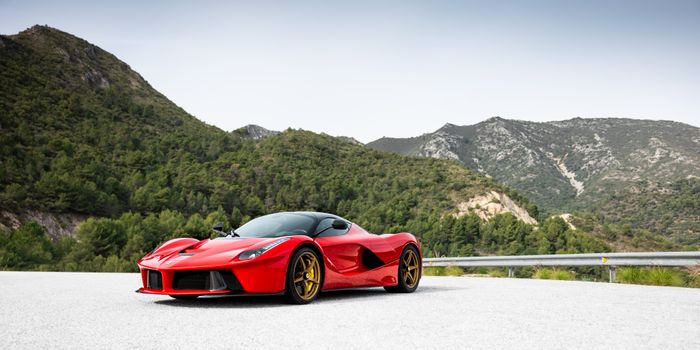 A striking red sports car parked on a mountain road surrounded by lush greenery.
